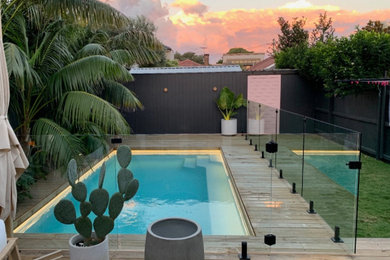 Diseño de piscina tropical de tamaño medio rectangular en patio trasero con paisajismo de piscina y entablado