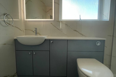 Design ideas for a medium sized modern shower room bathroom in Hampshire with flat-panel cabinets, blue cabinets, a walk-in shower, a one-piece toilet, white tiles, vinyl flooring, an integrated sink, quartz worktops, an open shower, white worktops, a single sink and a built in vanity unit.