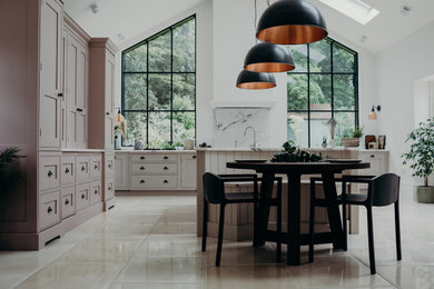 Photo of a large country u-shaped kitchen/diner in Surrey with a built-in sink, beaded cabinets, pink cabinets, marble worktops, white splashback, marble splashback, stainless steel appliances, limestone flooring, an island, beige floors, white worktops, a vaulted ceiling and a feature wall.