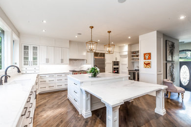 Inspiration for a large u-shaped open plan kitchen in Calgary with an undermount sink, shaker cabinets, white cabinets, marble benchtops, white splashback, marble splashback, stainless steel appliances, medium hardwood floors, with island, brown floor and white benchtop.
