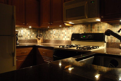 Example of a small trendy l-shaped laminate floor and brown floor eat-in kitchen design in Philadelphia with a single-bowl sink, raised-panel cabinets, dark wood cabinets, granite countertops, multicolored backsplash, stone tile backsplash and colored appliances