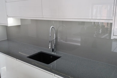 This is an example of a large contemporary open plan kitchen in Other with flat-panel cabinets, white cabinets, quartz benchtops, grey splashback, glass sheet splashback and with island.