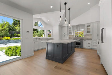 Inspiration for a large modern medium tone wood floor, beige floor and vaulted ceiling open concept kitchen remodel in San Francisco with an undermount sink, recessed-panel cabinets, white cabinets, quartzite countertops, multicolored backsplash, stone slab backsplash, paneled appliances, an island and multicolored countertops