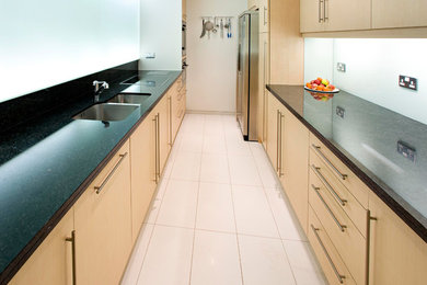Design ideas for a small contemporary galley enclosed kitchen in London with a double-bowl sink, light wood cabinets, wood worktops, black splashback, no island, yellow floors and beige worktops.