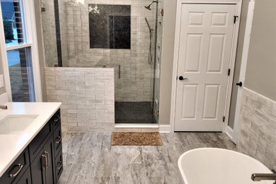 This is an example of a large modern master bathroom in Other with shaker cabinets, dark wood cabinets, a freestanding tub, an alcove shower, gray tile, ceramic tile, grey walls, ceramic floors, an undermount sink, engineered quartz benchtops, grey floor, a hinged shower door, white benchtops, a niche, a double vanity and a freestanding vanity.