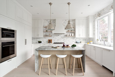 This is an example of a mid-sized transitional u-shaped eat-in kitchen in Vancouver with an undermount sink, shaker cabinets, white cabinets, quartzite benchtops, grey splashback, marble splashback, stainless steel appliances, with island, beige floor and white benchtop.