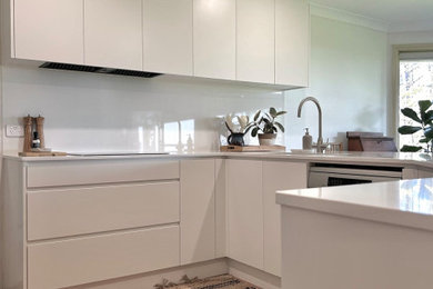 Design ideas for a mid-sized modern u-shaped separate kitchen in Sydney with an undermount sink, flat-panel cabinets, white cabinets, quartz benchtops, white splashback, engineered quartz splashback, stainless steel appliances, ceramic floors and white benchtop.