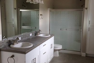 Inspiration for a mid-sized transitional 3/4 porcelain tile and brown floor bathroom remodel in Other with shaker cabinets, white cabinets, beige walls, a drop-in sink, concrete countertops and gray countertops