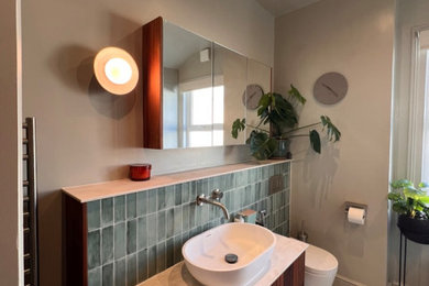 Photo of a medium sized modern grey and cream bathroom in Sussex with flat-panel cabinets, dark wood cabinets, a walk-in shower, a wall mounted toilet, green tiles, porcelain tiles, green walls, porcelain flooring, a pedestal sink, engineered stone worktops, grey floors, an open shower, beige worktops, feature lighting, a single sink and a floating vanity unit.