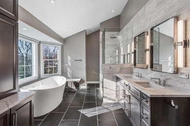 Example of a large trendy master gray tile and limestone tile slate floor, black floor, double-sink and vaulted ceiling bathroom design in Chicago with flat-panel cabinets, medium tone wood cabinets, a one-piece toilet, gray walls, an undermount sink, quartz countertops, a hinged shower door, white countertops, a niche and a built-in vanity