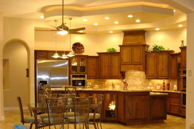 Photo of a large traditional l-shaped separate kitchen in Phoenix with an undermount sink, raised-panel cabinets, dark wood cabinets, granite benchtops, beige splashback, travertine splashback, stainless steel appliances, porcelain floors, with island, beige floor and beige benchtop.
