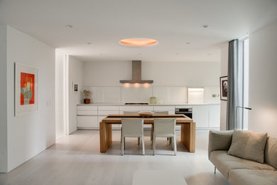 Large modern single-wall eat-in kitchen in San Francisco with white splashback, glass sheet splashback, light hardwood floors, beige floor, an integrated sink, flat-panel cabinets, white cabinets, stainless steel benchtops, stainless steel appliances and no island.
