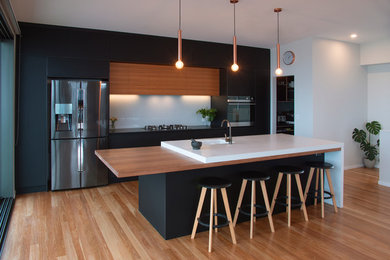 This is an example of a mid-sized contemporary galley open plan kitchen in Newcastle - Maitland with an undermount sink, flat-panel cabinets, concrete benchtops, white splashback, glass sheet splashback, stainless steel appliances, medium hardwood floors, with island, brown floor and grey benchtop.