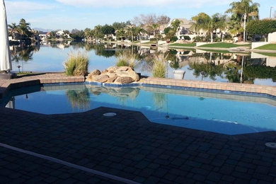 Inspiration for a mid-sized traditional backyard custom-shaped pool in Phoenix with brick pavers.