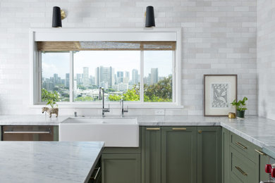 Example of a large transitional u-shaped medium tone wood floor and brown floor kitchen pantry design in Hawaii with a farmhouse sink, shaker cabinets, green cabinets, marble countertops, white backsplash, ceramic backsplash, stainless steel appliances, an island and gray countertops