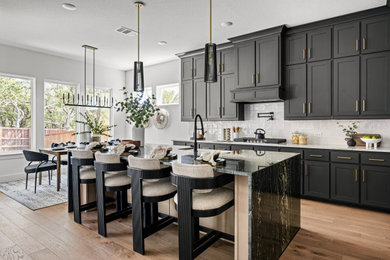 Example of a large transitional l-shaped medium tone wood floor and brown floor open concept kitchen design in Dallas with a farmhouse sink, recessed-panel cabinets, black cabinets, marble countertops, white backsplash, ceramic backsplash, an island and black countertops