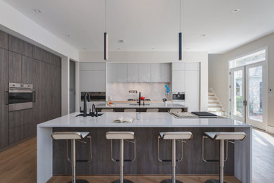 Example of a huge trendy l-shaped light wood floor and beige floor open concept kitchen design in DC Metro with an undermount sink, flat-panel cabinets, white cabinets, quartz countertops, white backsplash, quartz backsplash, paneled appliances, two islands and white countertops