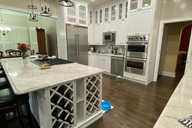 Example of a large minimalist galley dark wood floor and brown floor eat-in kitchen design in Atlanta with a drop-in sink, raised-panel cabinets, white cabinets, quartz countertops, stainless steel appliances, an island and multicolored countertops