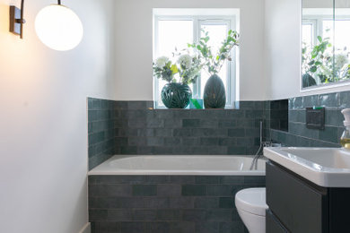 Medium sized family bathroom in London with flat-panel cabinets, green cabinets, a built-in bath, a built-in shower, a one-piece toilet, green tiles, ceramic tiles, white walls, mosaic tile flooring, a built-in sink, multi-coloured floors, a sliding door, white worktops, a single sink and a floating vanity unit.