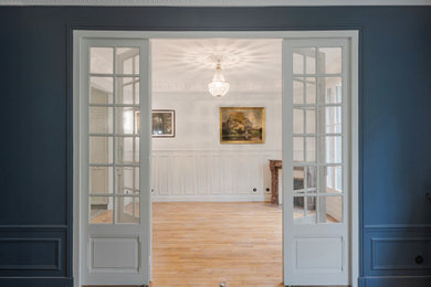 Aménagement d'une salle à manger ouverte sur le salon avec un mur bleu, parquet clair et une cheminée d'angle.