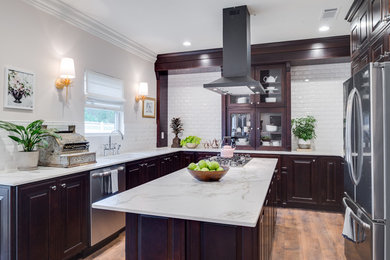 Mid-sized transitional l-shaped eat-in kitchen in Orange County with an undermount sink, raised-panel cabinets, dark wood cabinets, marble benchtops, white splashback, subway tile splashback, stainless steel appliances, medium hardwood floors and with island.