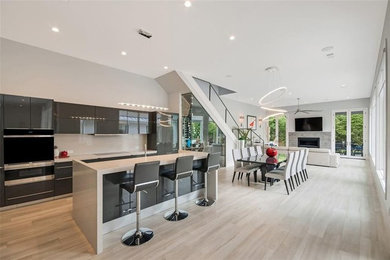 Mid-sized trendy single-wall light wood floor and brown floor open concept kitchen photo in Houston with an undermount sink, flat-panel cabinets, gray cabinets, solid surface countertops, beige backsplash, stone slab backsplash, stainless steel appliances, an island and beige countertops