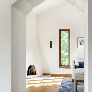 Ejemplo de salón mediterráneo, grande, con paredes blancas, suelo de madera clara, chimenea de esquina, marco de chimenea de yeso y suelo marrón