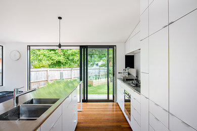 Contemporary galley eat-in kitchen in Christchurch with white cabinets, with island, a double-bowl sink, stainless steel benchtops, white splashback, ceramic splashback, stainless steel appliances, medium hardwood floors and multi-coloured floor.