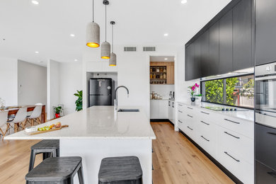 Design ideas for a large contemporary single-wall kitchen pantry in Brisbane with an undermount sink, white cabinets, quartz benchtops, window splashback, stainless steel appliances, medium hardwood floors, with island and white benchtop.
