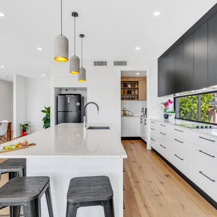 Design ideas for a large contemporary single-wall kitchen pantry in Brisbane with an undermount sink, white cabinets, quartz benchtops, window splashback, stainless steel appliances, medium hardwood floors, with island and white benchtop.