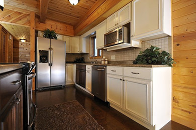 Example of a mid-sized mountain style l-shaped dark wood floor and brown floor kitchen design in Other with an undermount sink, recessed-panel cabinets, white cabinets, granite countertops, white backsplash, ceramic backsplash, stainless steel appliances and an island
