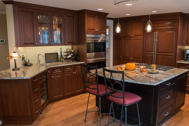 This is an example of a traditional kitchen in Seattle with a single-bowl sink, raised-panel cabinets, dark wood cabinets, granite benchtops, beige splashback, stone tile splashback, stainless steel appliances, medium hardwood floors and with island.