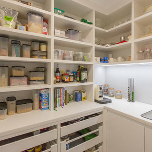 Idées déco pour une grande arrière-cuisine contemporaine en U avec un évier encastré, un placard à porte plane, des portes de placard blanches, un plan de travail en surface solide, un électroménager en acier inoxydable, béton au sol, une crédence grise et une crédence en feuille de verre.