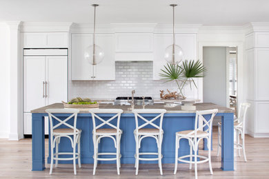 Inspiration for a coastal medium tone wood floor and brown floor open concept kitchen remodel in Other with a farmhouse sink, recessed-panel cabinets, white cabinets, wood countertops, white backsplash, subway tile backsplash, paneled appliances, an island and brown countertops