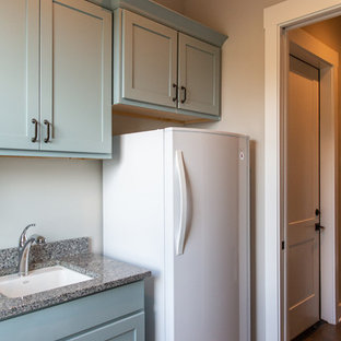 オースティンの中サイズのカントリー風おしゃれな洗濯室 (アンダーカウンターシンク、シェーカースタイル扉のキャビネット、青いキャビネット、御影石カウンター、グレーの壁、磁器タイルの床、左右配置の洗濯機・乾燥機、茶色い床、マルチカラーのキッチンカウンター) の写真