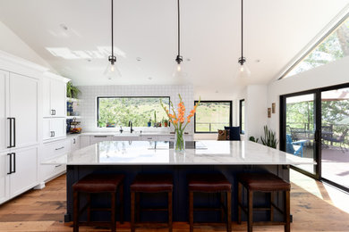 Southwest medium tone wood floor, brown floor and vaulted ceiling kitchen photo in Denver with a farmhouse sink, shaker cabinets, white cabinets, quartz countertops, white backsplash, mosaic tile backsplash, paneled appliances, an island and gray countertops