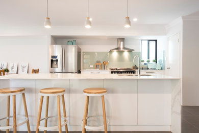 Design ideas for a large modern single-wall open plan kitchen in Perth with an undermount sink, white cabinets, solid surface benchtops, green splashback, glass sheet splashback, stainless steel appliances, ceramic floors and with island.