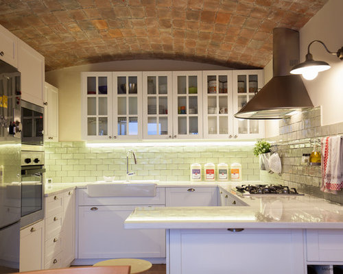 Diseño de cocina en U, clásica renovada, con puertas de armario blancas, electrodomésticos de acero inoxidable, península, fregadero sobremueble, armarios tipo vitrina y salpicadero de azulejos tipo metro