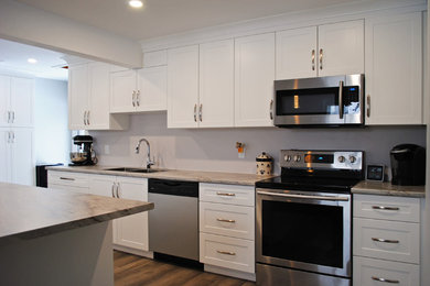 Example of a mid-sized transitional medium tone wood floor and brown floor kitchen pantry design in Other with a drop-in sink, shaker cabinets, white cabinets, laminate countertops, beige backsplash, stainless steel appliances, an island and gray countertops