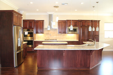 Kitchen - large traditional l-shaped dark wood floor and brown floor kitchen idea in Sacramento with an undermount sink, raised-panel cabinets, dark wood cabinets, granite countertops, beige backsplash, stone tile backsplash, stainless steel appliances, two islands and beige countertops