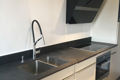 Réalisation d'une petite cuisine linéaire et encastrable minimaliste fermée avec un évier intégré, un plan de travail en granite, une crédence noire et tomettes au sol.