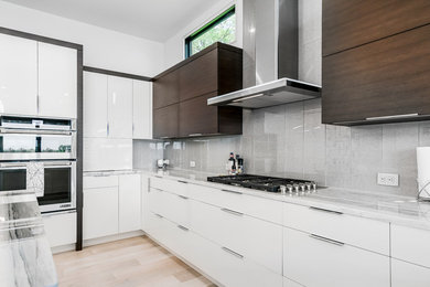 Example of a trendy light wood floor kitchen design in Grand Rapids with flat-panel cabinets, quartz countertops, glass tile backsplash, stainless steel appliances and an island