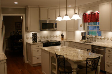 This is an example of a traditional u-shaped eat-in kitchen in Chicago with an undermount sink, recessed-panel cabinets, white cabinets, granite benchtops, white splashback, porcelain splashback and stainless steel appliances.