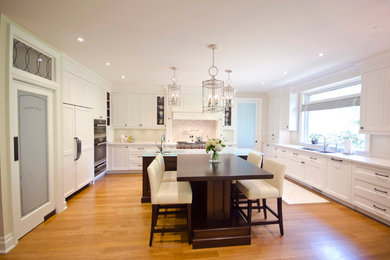 Design ideas for a large transitional u-shaped open plan kitchen in Toronto with a double-bowl sink, beaded inset cabinets, white cabinets, quartzite benchtops, white splashback, glass sheet splashback, stainless steel appliances and light hardwood floors.