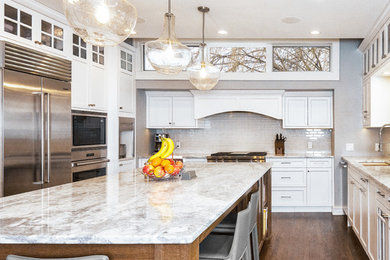Transitional dark wood floor and brown floor kitchen photo in Minneapolis with an undermount sink, shaker cabinets, white cabinets, quartzite countertops, white backsplash, glass tile backsplash, stainless steel appliances, an island and white countertops