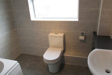 This is an example of a mid-sized contemporary kids bathroom in Other with flat-panel cabinets, grey cabinets, a two-piece toilet, gray tile, ceramic tile, grey walls, ceramic floors and laminate benchtops.