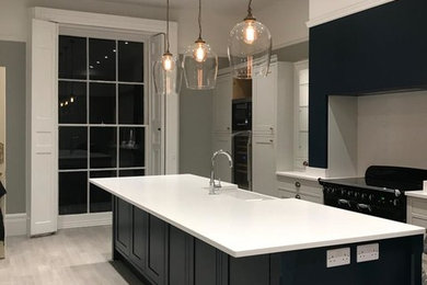 Inspiration for an expansive contemporary u-shaped open plan kitchen in Essex with a farmhouse sink, shaker cabinets, blue cabinets, marble benchtops, light hardwood floors, with island, white floor and white benchtop.