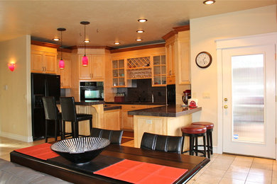 Example of a mid-sized trendy u-shaped travertine floor open concept kitchen design in Other with an undermount sink, glass-front cabinets, light wood cabinets, black backsplash, stone tile backsplash, black appliances, two islands and granite countertops