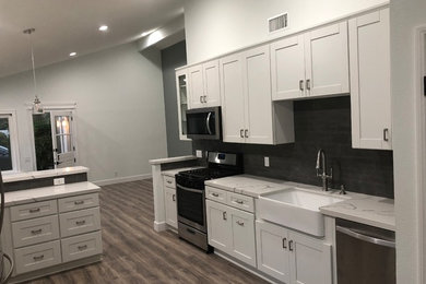 Eat-in kitchen - mid-sized traditional galley laminate floor eat-in kitchen idea in Orange County with a farmhouse sink, shaker cabinets, ceramic backsplash, a peninsula, quartz countertops and gray backsplash