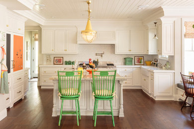 Elegant u-shaped medium tone wood floor eat-in kitchen photo in Los Angeles with a farmhouse sink, raised-panel cabinets, white cabinets, white backsplash, ceramic backsplash, paneled appliances and an island